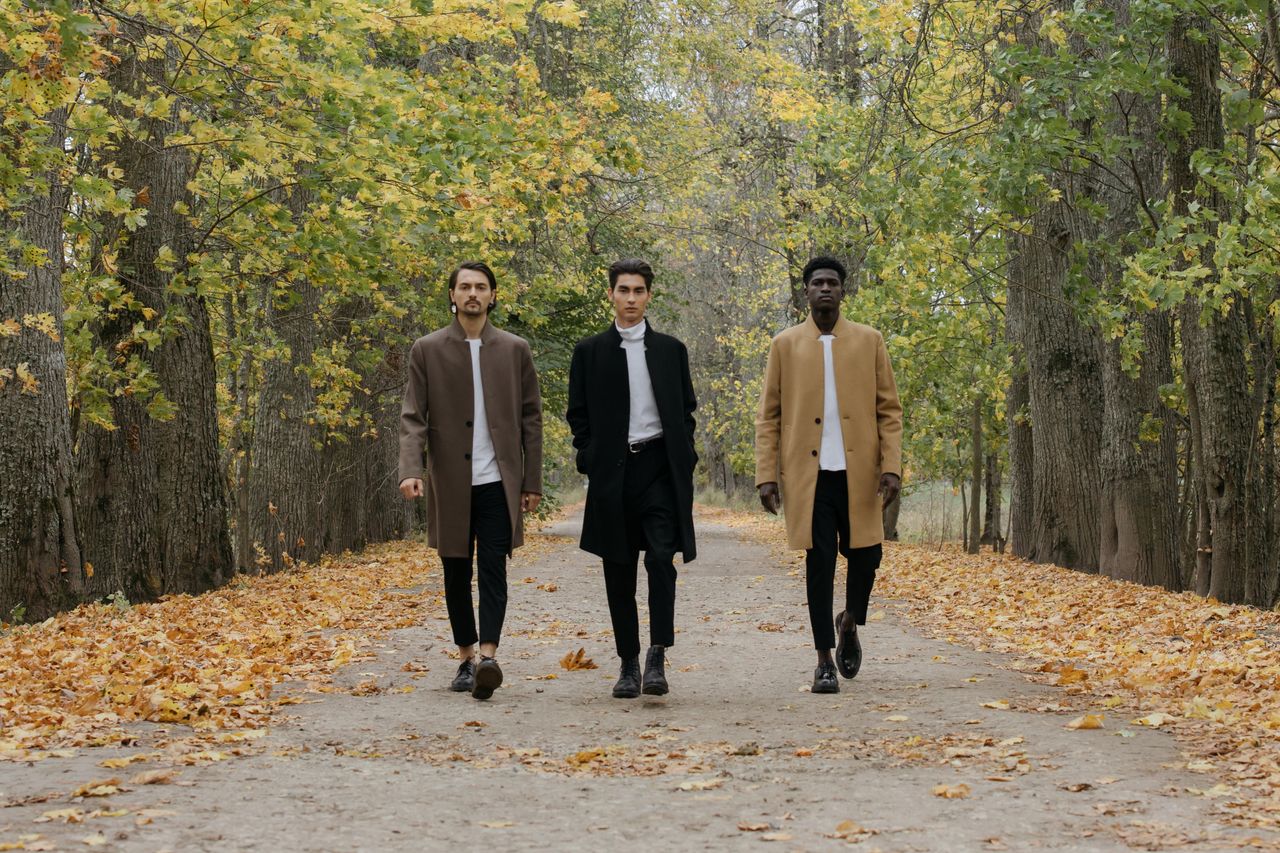 About Three stylish men walking down a leaf-covered path in an autumn park.